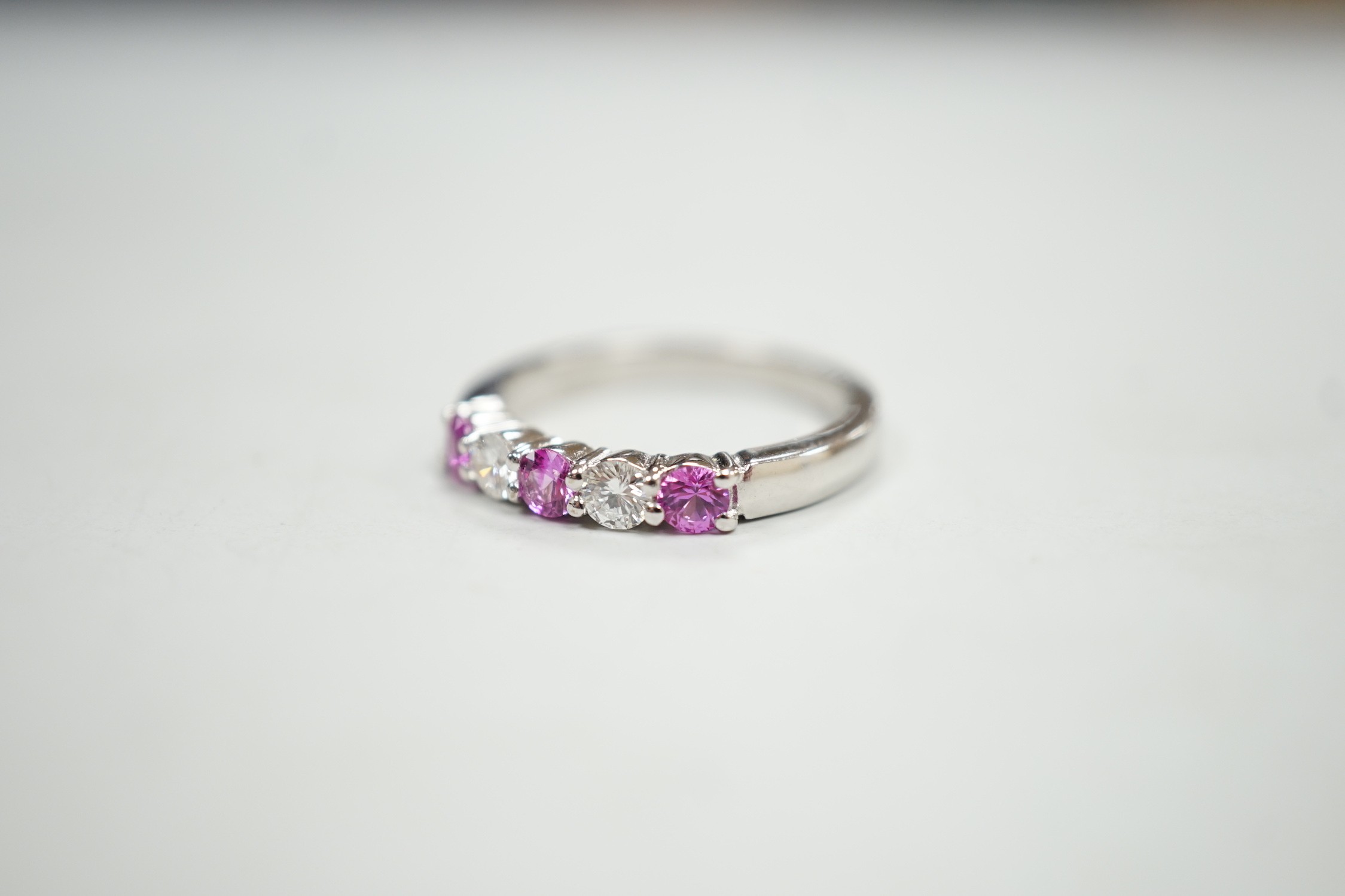 A modern 18ct white gold, three pink stone and two stone diamond set half hoop ring, size M, gross weight 4 grams.